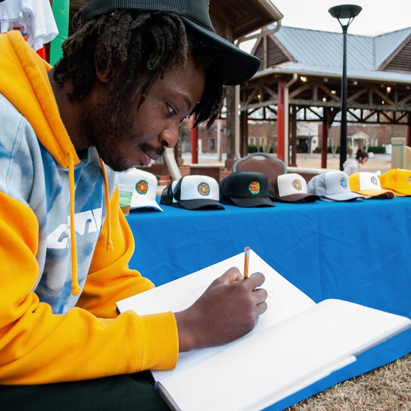 An artist drawing beside a table of hats at the festival