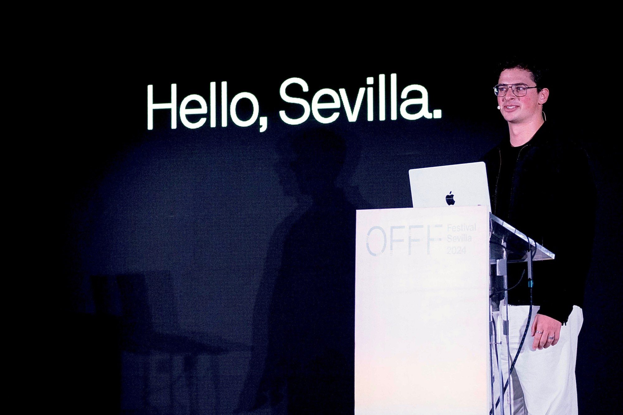 Eron at a podium beneath a slide reading “Hello, Sevilla.” at OFFF Festival Sevilla 2024