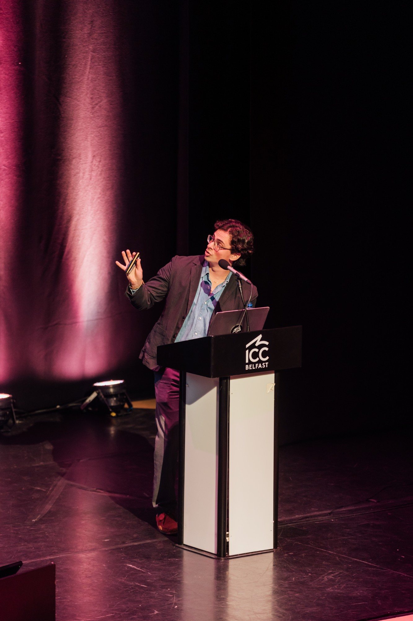Eron turning to gesture at the screen from the ICC Belfast podium