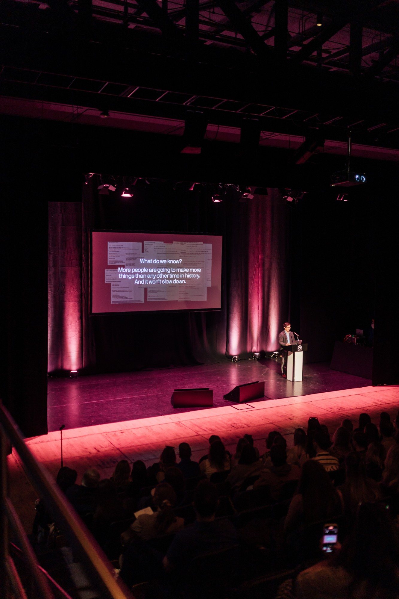 Eron on stage at ICC Belfast beneath a slide reading “What do we know?”