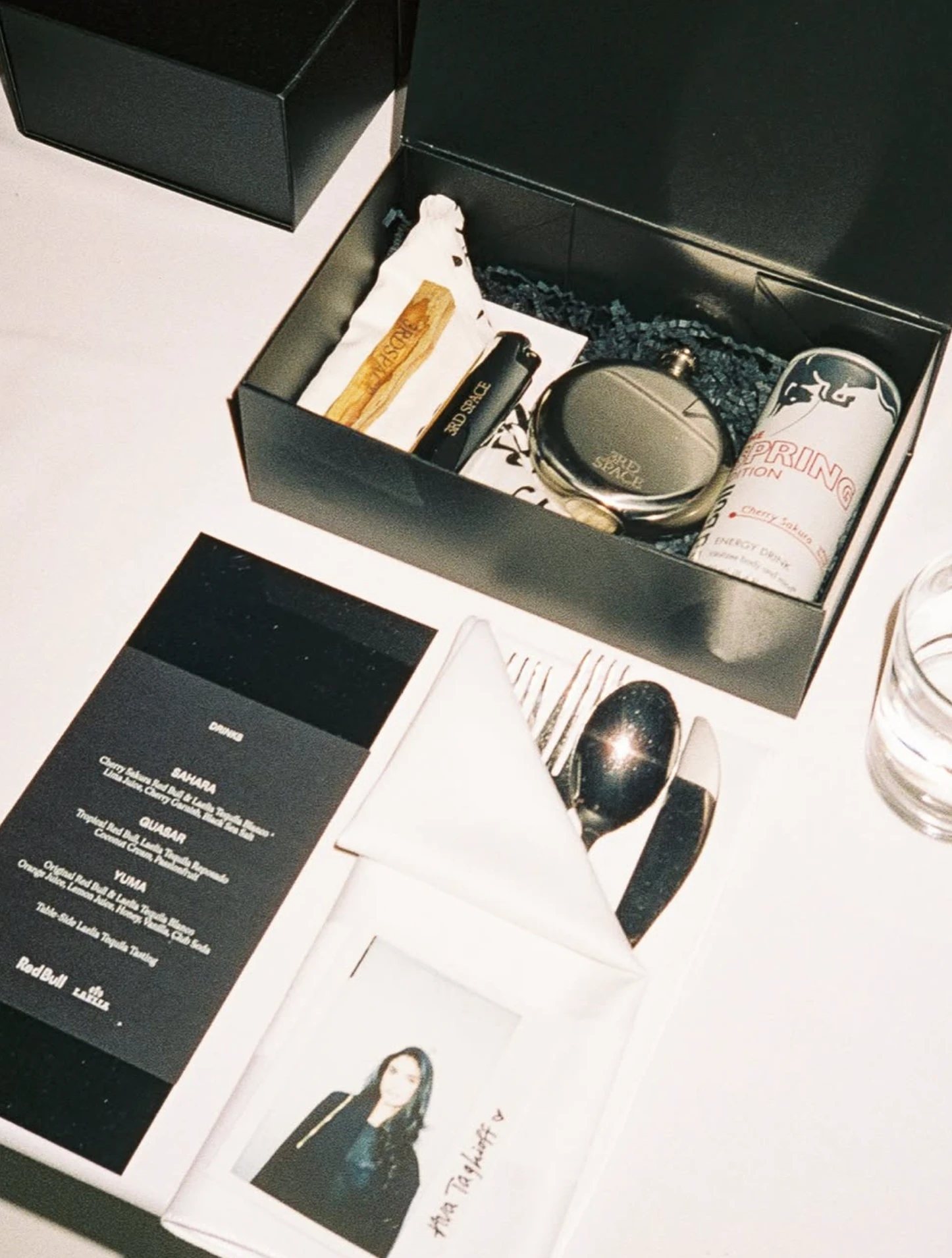 A gift box, drinks menu and polaroid place card at a table setting